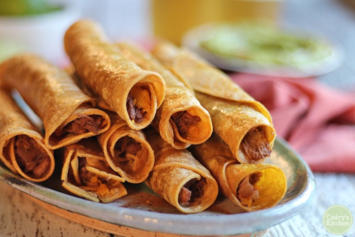 a pile of rolled taquitos sit on a grey plate