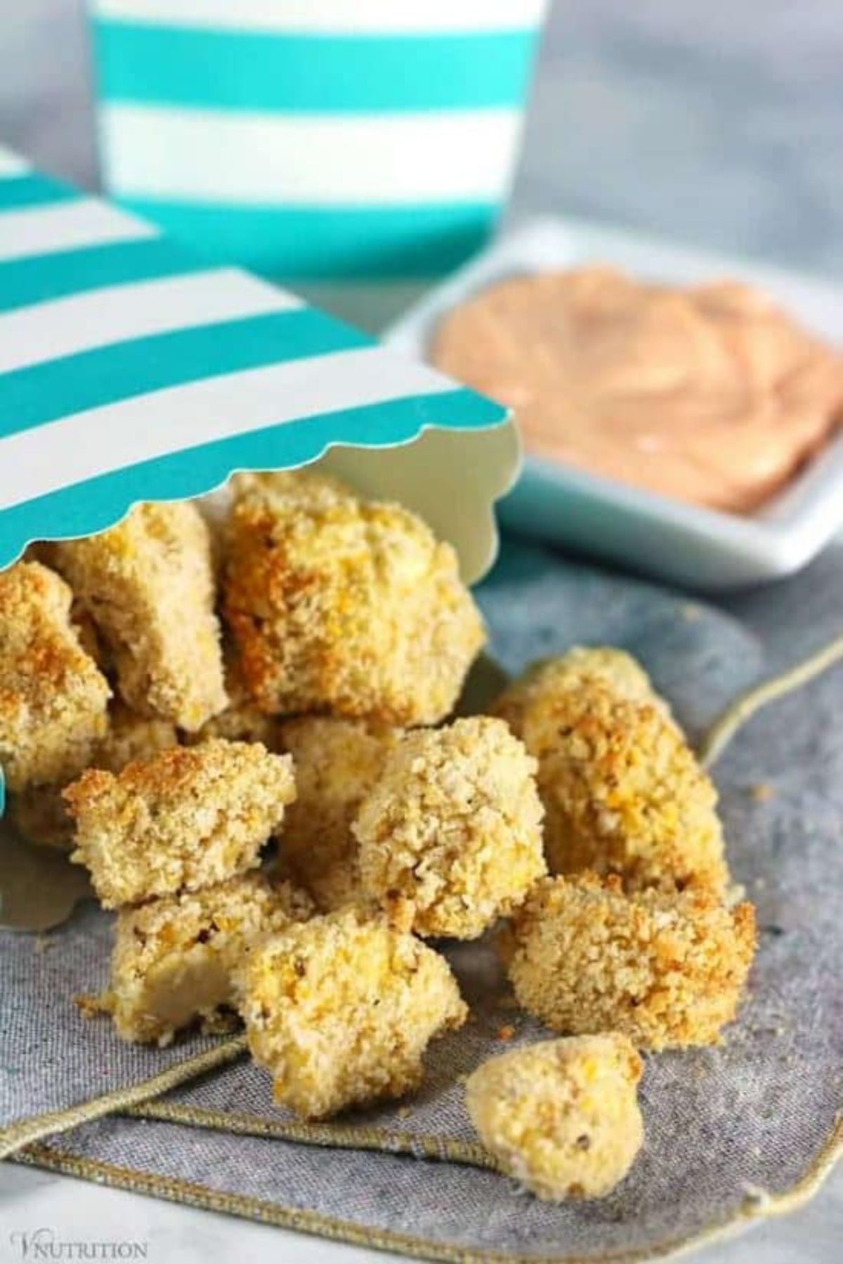 small air fried pieces of tofu fall out of a popcorn carton onto a gray cloth