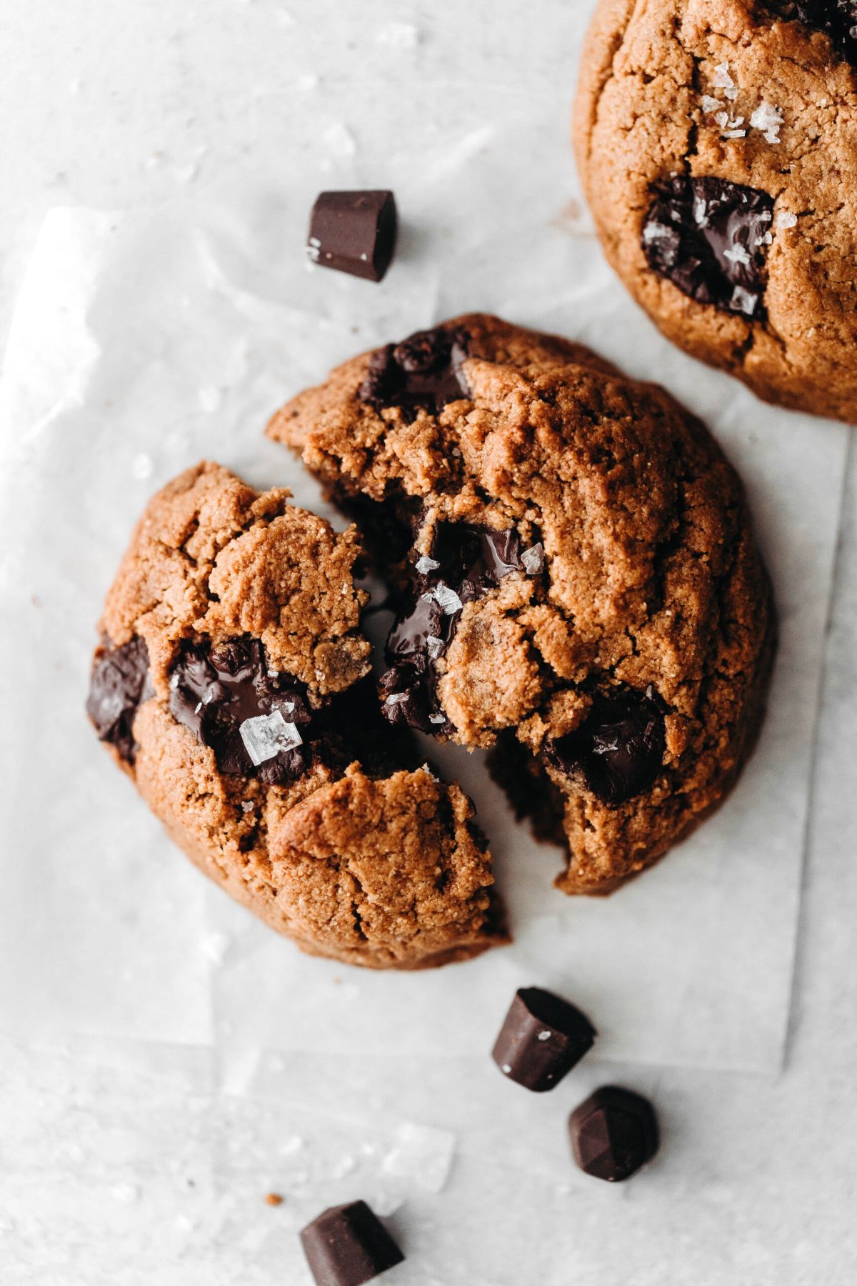 a vegan chocolate chip cookie broken in half, with chocolate chips scattered around