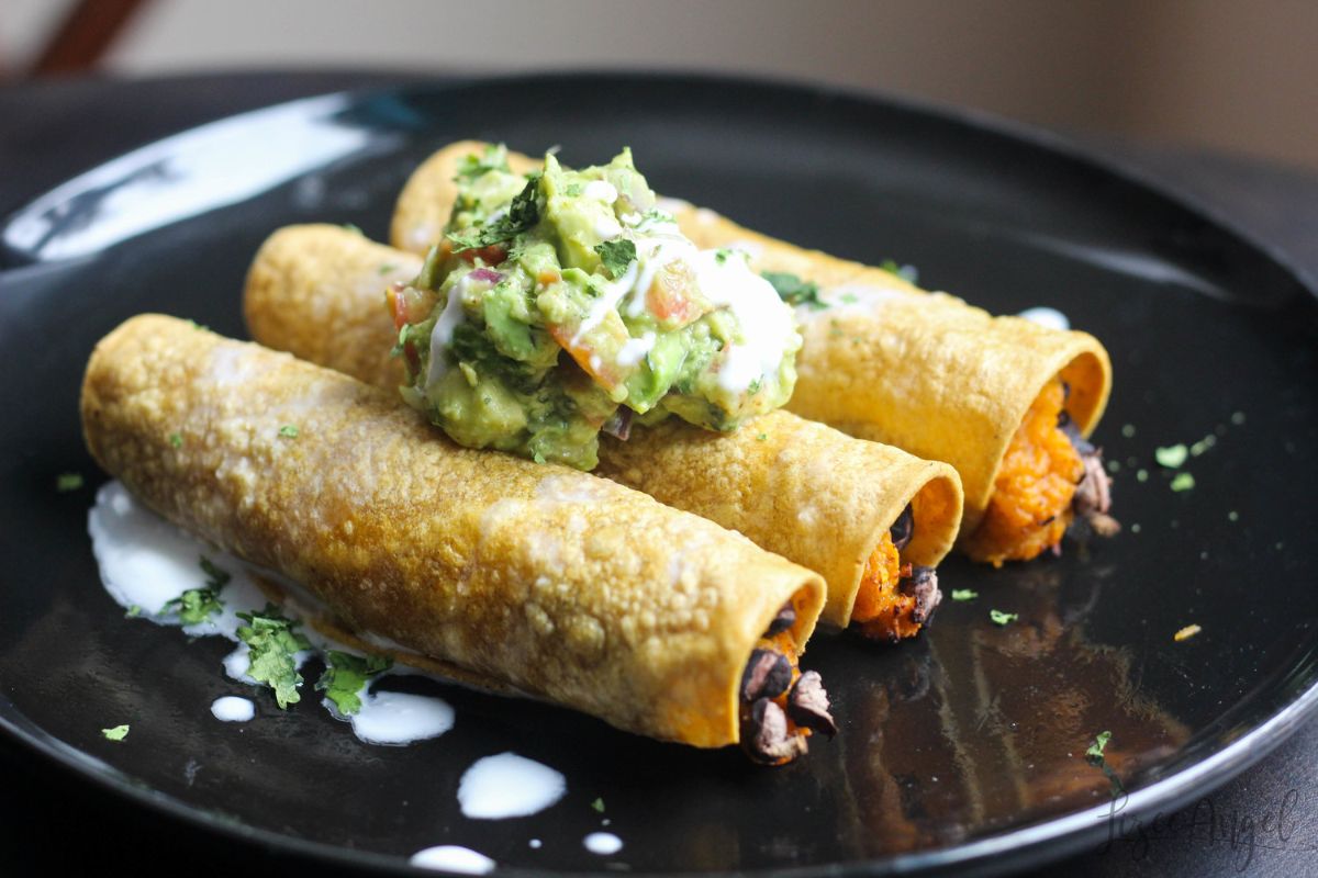 a black plate with 3 taquitos on it, topped with guacemole