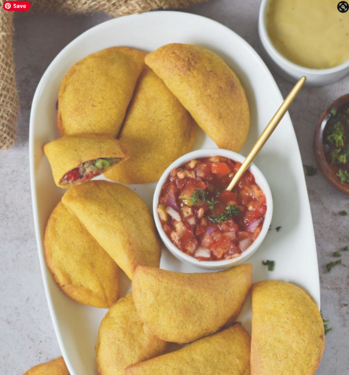 a white oval dish of empanadas with a bowl of salsa in the middle of the pile