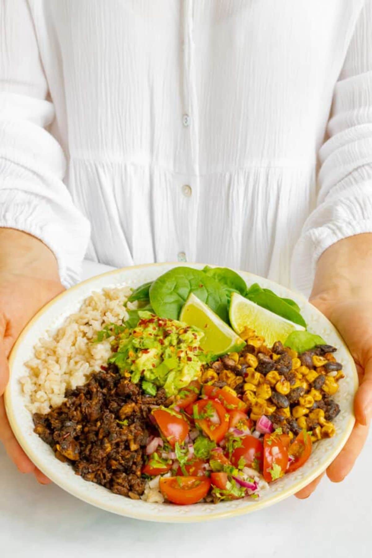 a woman in a white shirt holds a mushroom burrito bowl