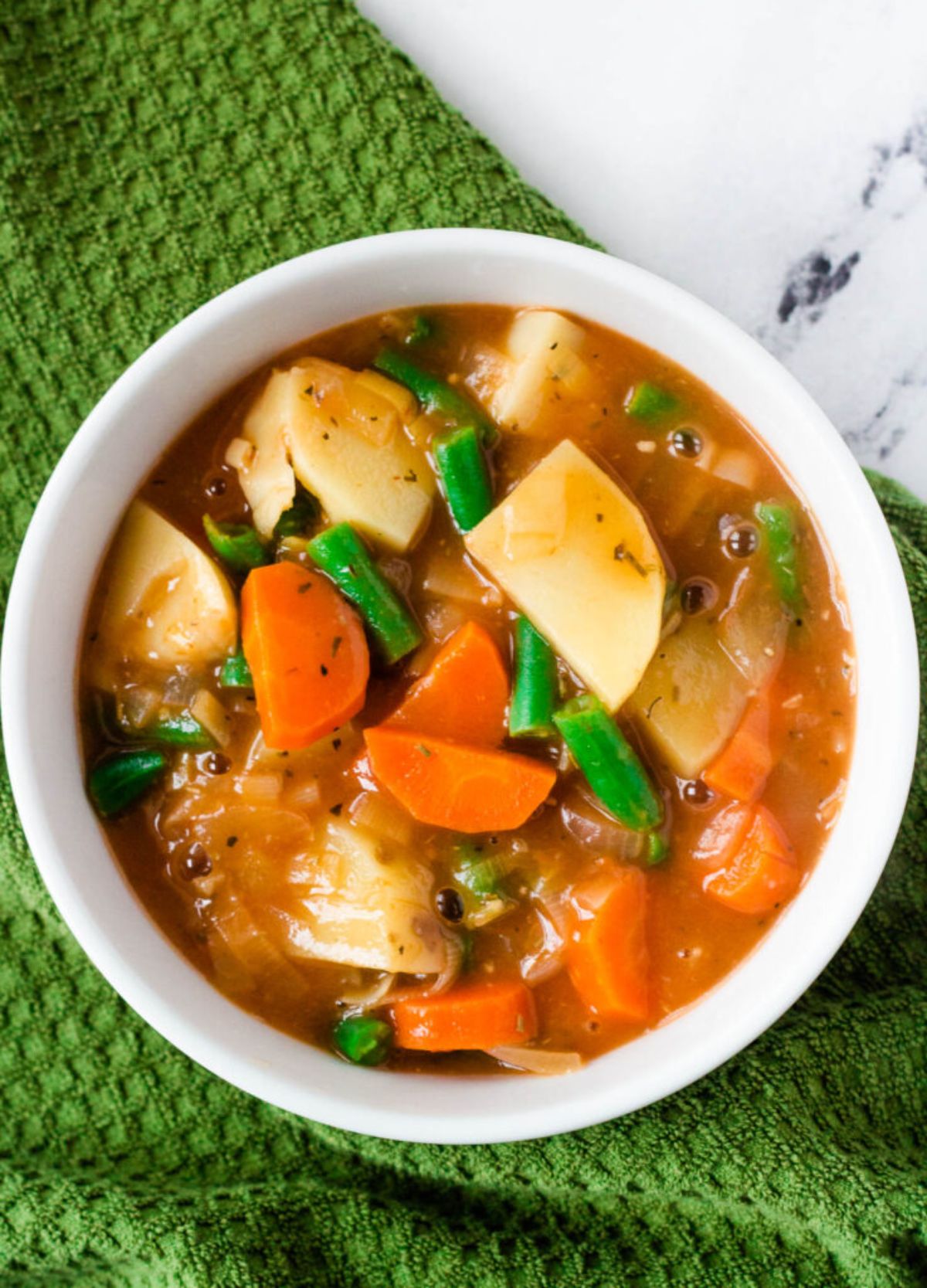 a white bowl full of vegetable stew on a green cloth