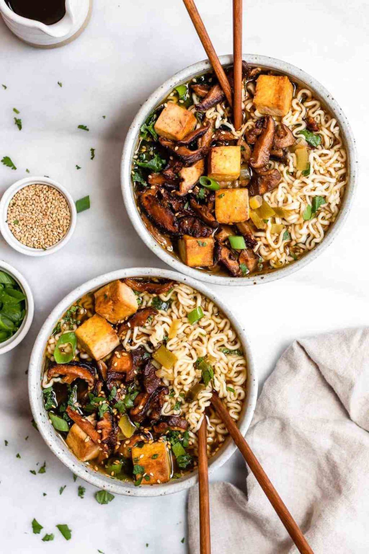 2 bowls full of ramen, topped with vegetables and tofu, with chopsticks sticking out of them