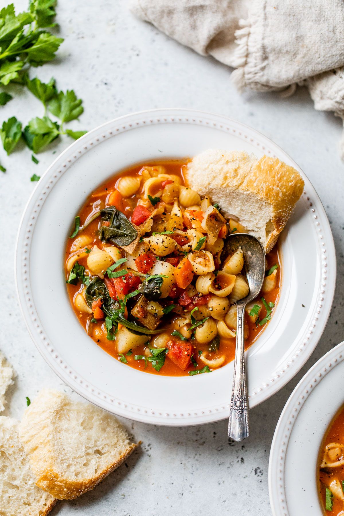 a white dish full of minestrone with a slice of bread on the side