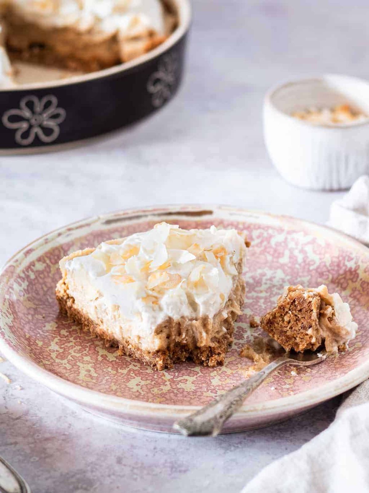 a plate with a slice of vegan coconut cream pie on it. a spoon has taken a piece out of it