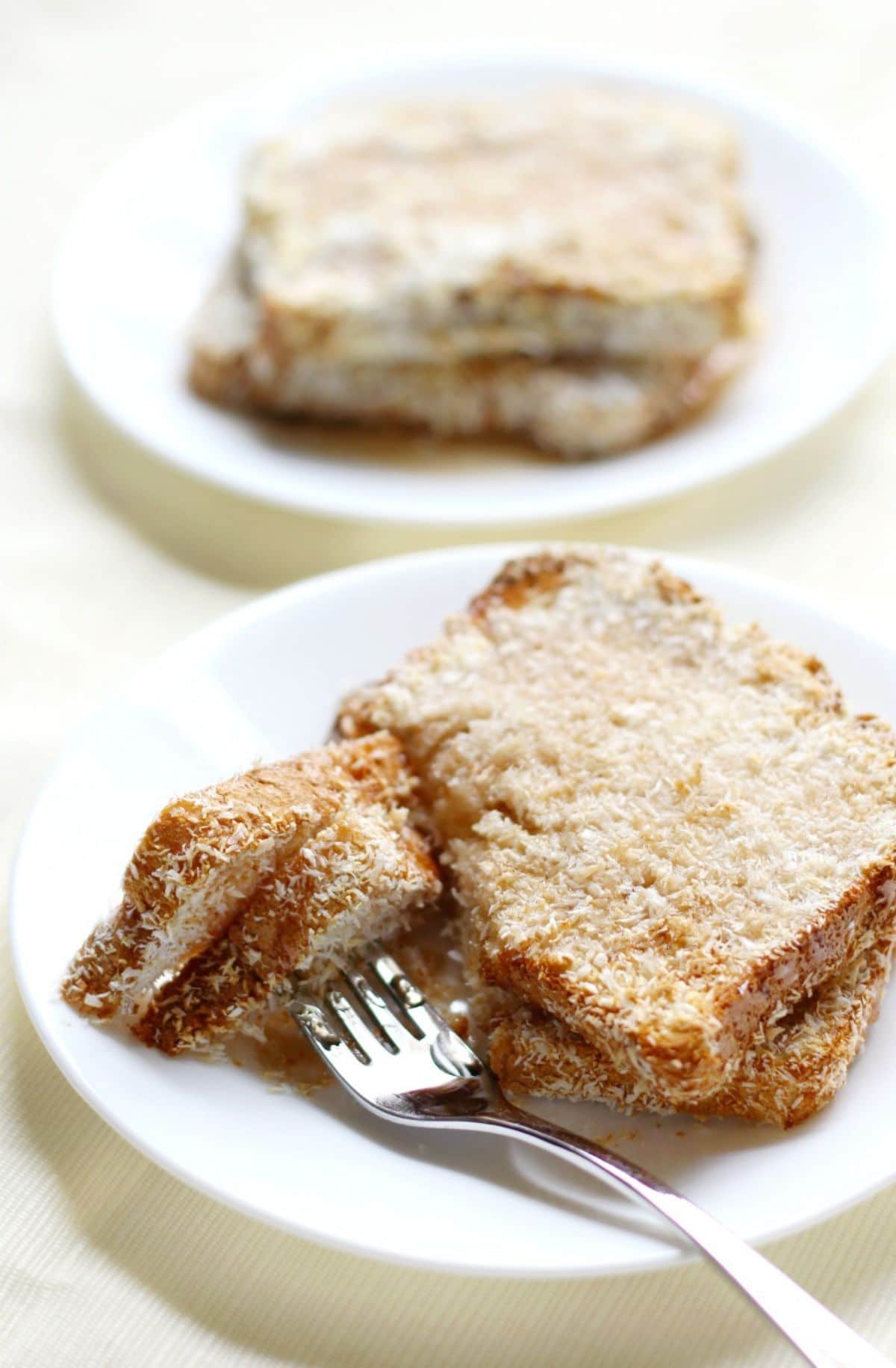 2 plates of coconut french toast. The nearest plate has a fork sticking into a portion of the slice