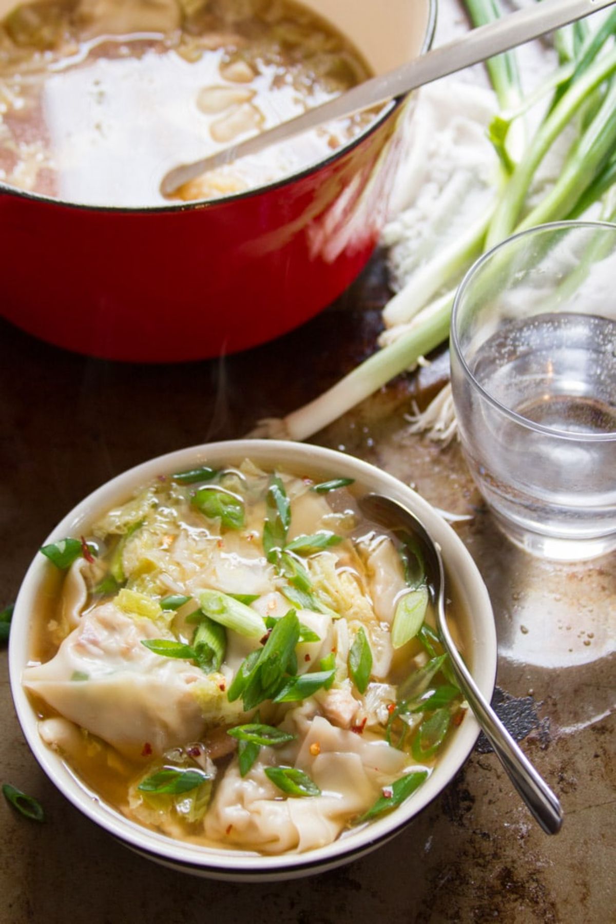 a casserole dish full of shiitake wonton soup with a bowl of the soup in front of it