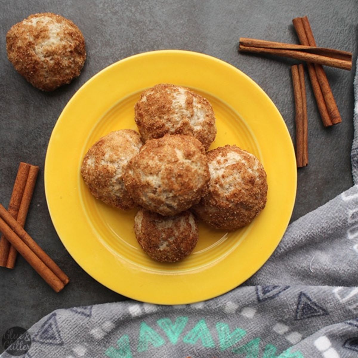 a yellow plate with churro donut holes on it. Cinnamon sticks are resting on either side