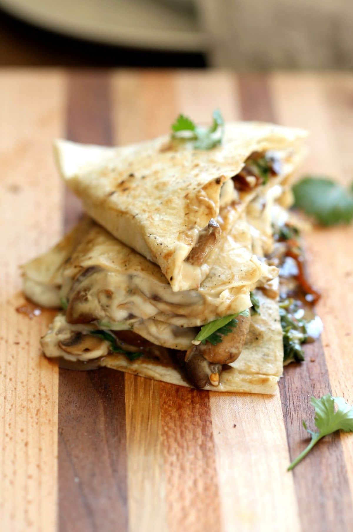 vegan mushroom quesadillas sit piled on a wooden board