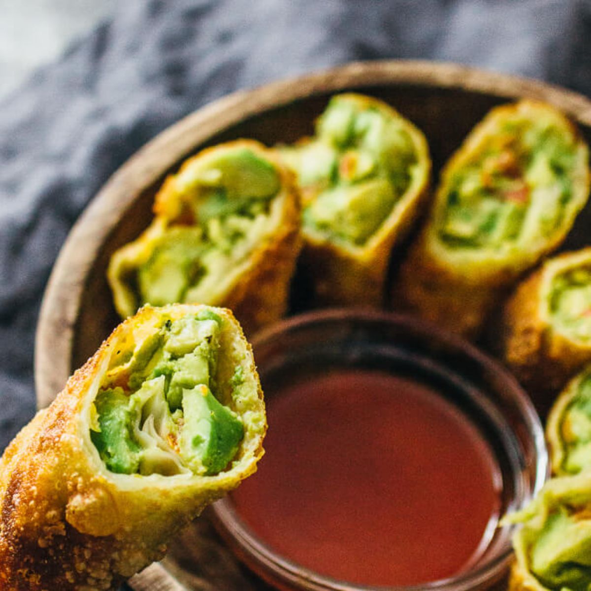 a close up of a bowl of vegan egg rolls filled with avocado surrounding a small bowl of red sauce
