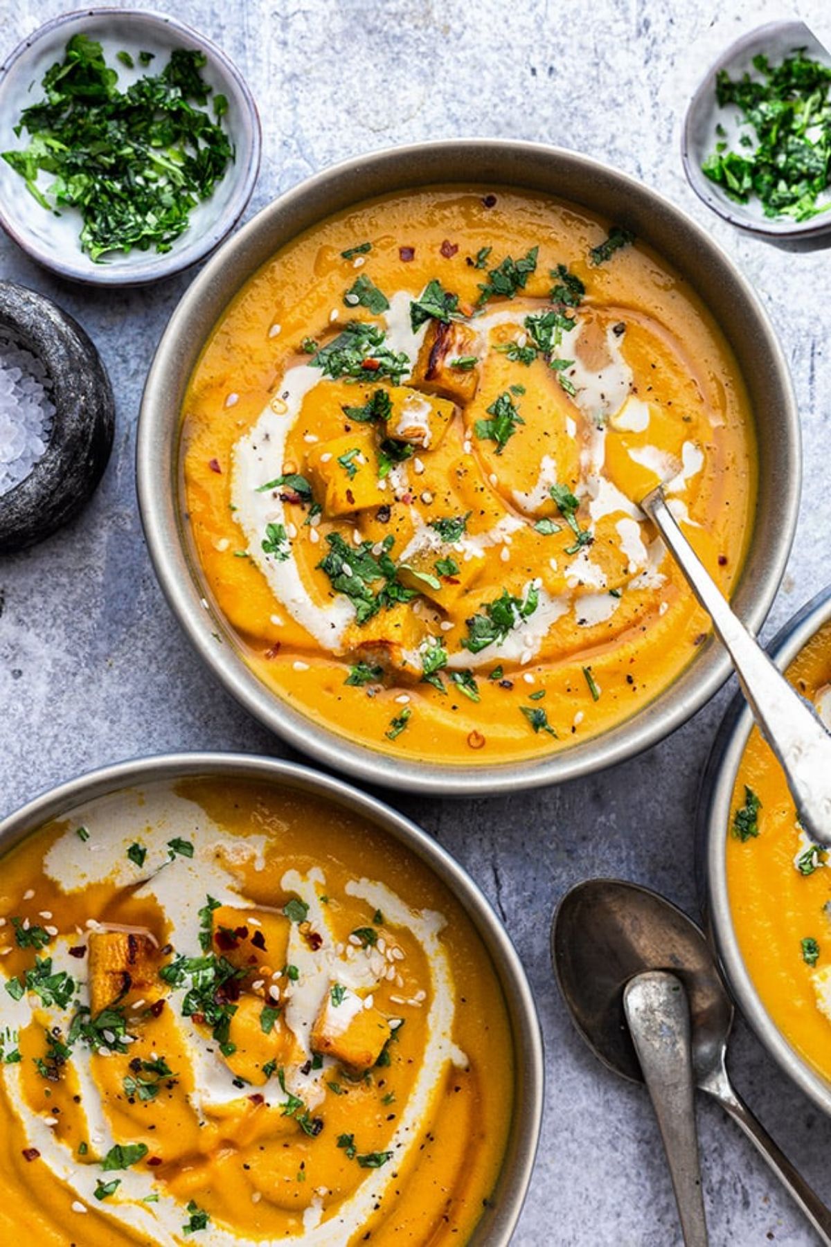 2 dishes filled with pumpkin soup, topped with scattered herbs and drizzled with cream