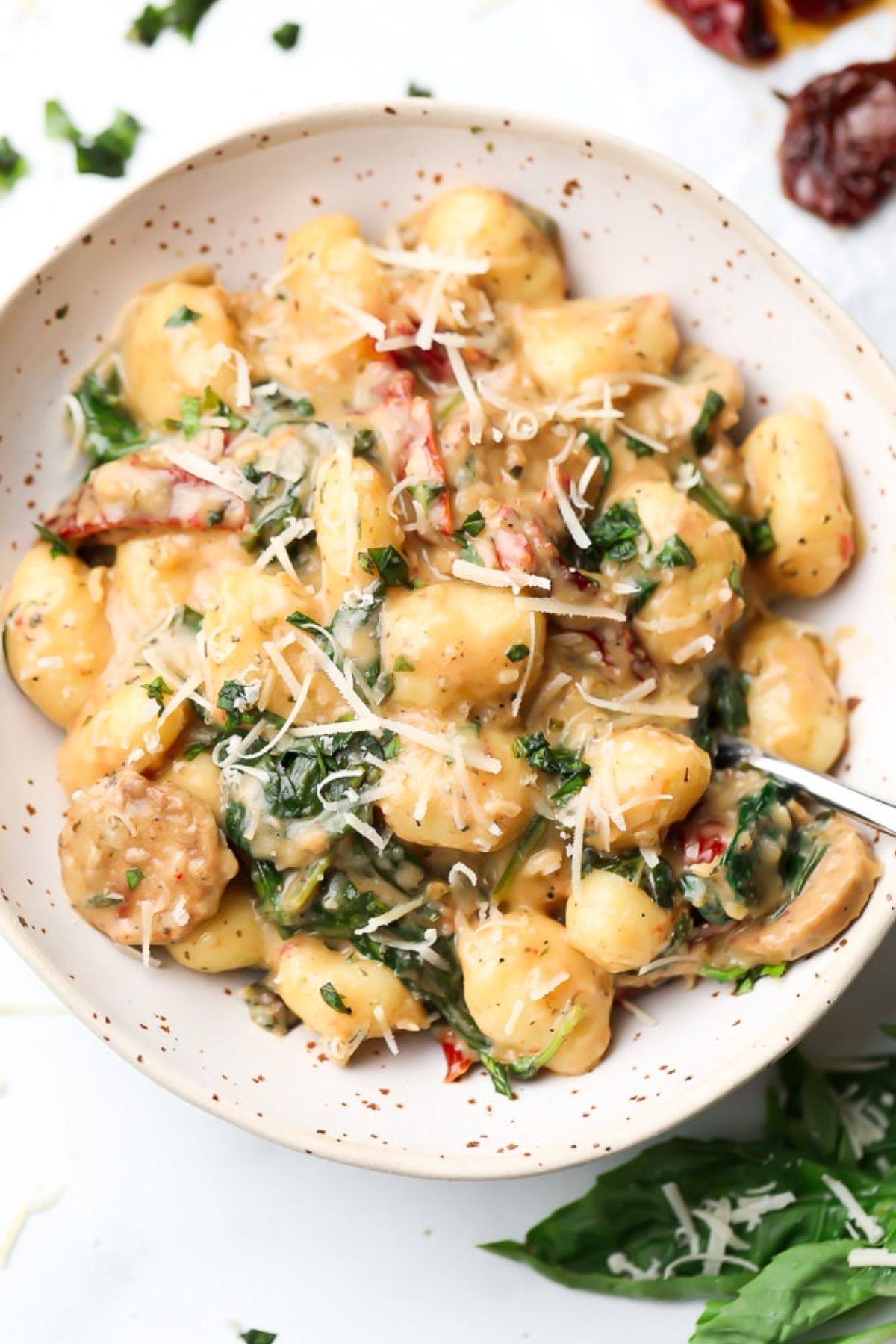 A bowl of tuscan vegan gnocchi topped with grated vegan cheese and herbs