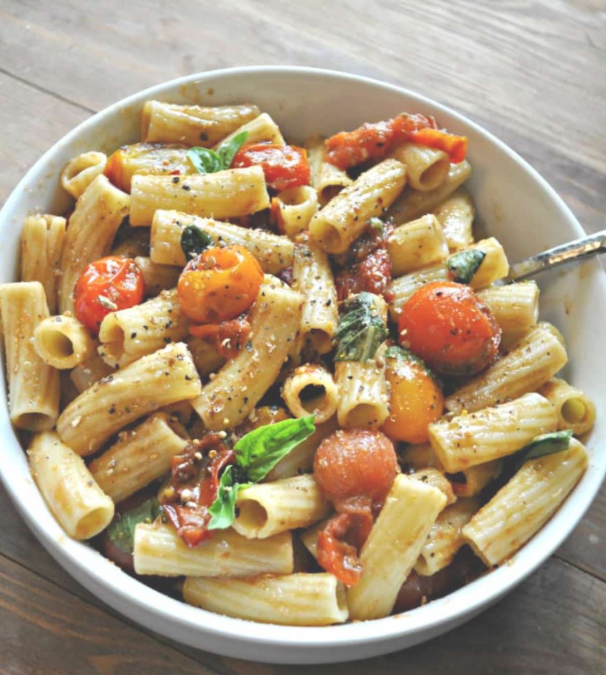 A bowl of vegan bruschetta pasta topped with fresh basil