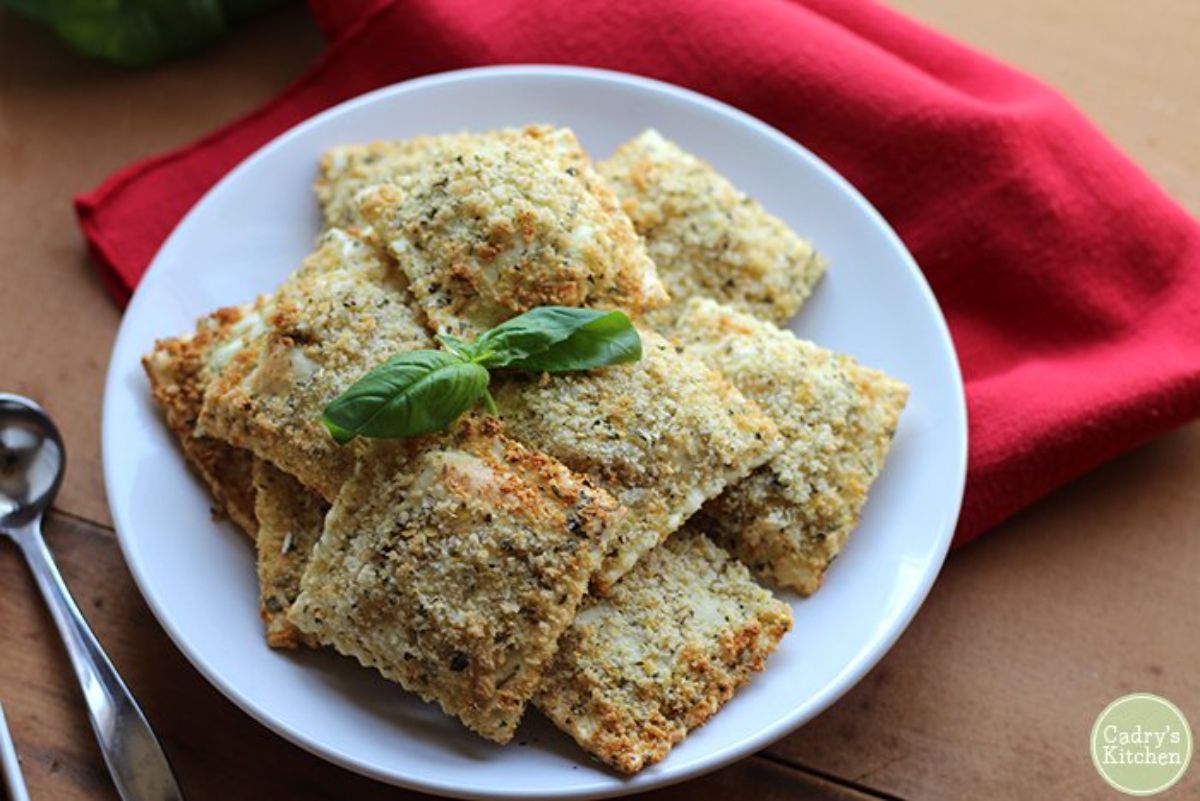 a white plate of filled ravioli topped with a basil sprig. The plate sits on a table and a red cloth