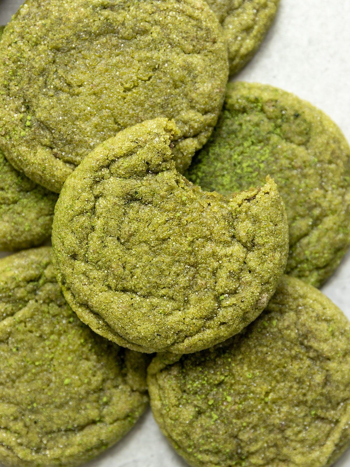 a pile of matcha sugar cookies. the top one has a bite taken out of it