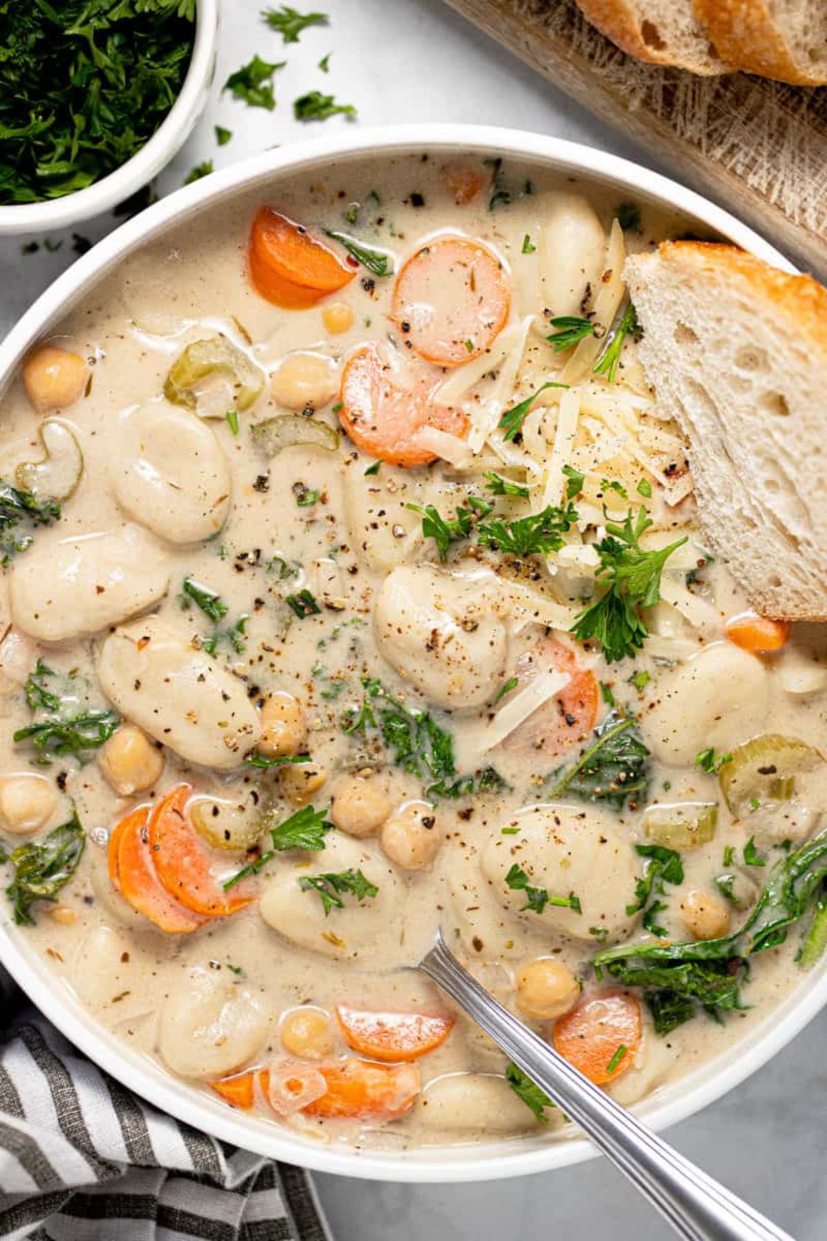 a white bowl full of gnocchi soup and vegetables. a slice of bread is on top