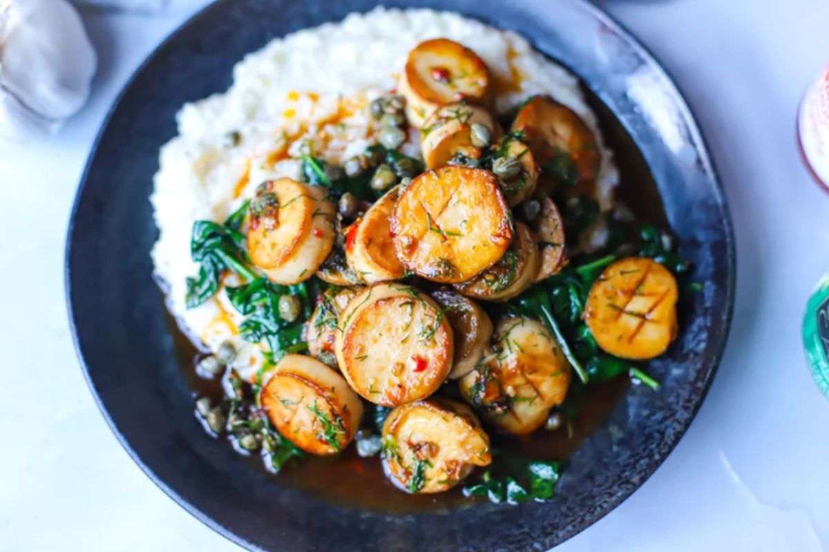 a black plate of king oyster scallops, wilted spinach and mash