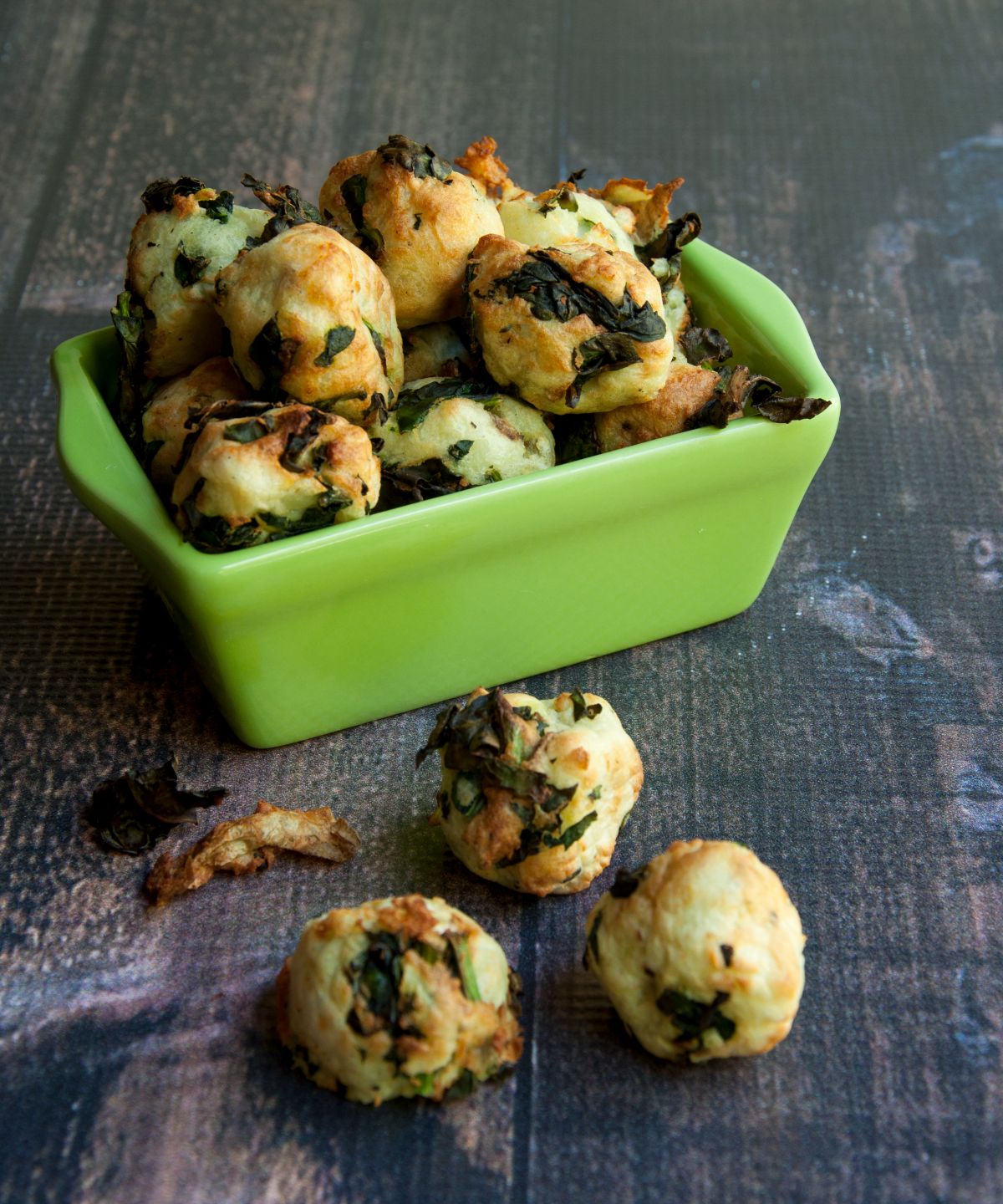 a green square casserole dish filled with potato and kale nuggets. Some have spilled out onto the gray surface